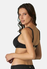 Reggiseno nero con una fantasia a pois, dotato di spalline regolabili, scollatura profonda e dettagli dorati sulle spalline.