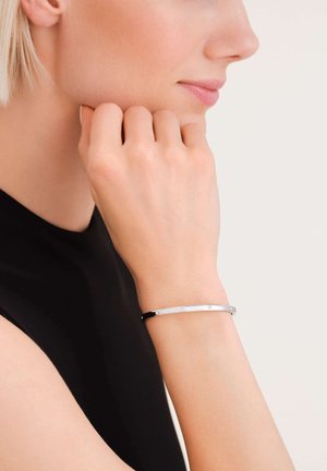 Silberner und schwarzer Armreif an einem Handgelenk, mit einer glatten metallischen Oberfläche, minimalistischen Design und kleinen Akzenten.