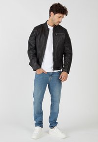 Zwarte leren bomberjack met een ritssluiting, geribbelde schouderaccenten, gedragen over een wit T-shirt, gecombineerd met lichtblauwe jeans en witte sneakers.