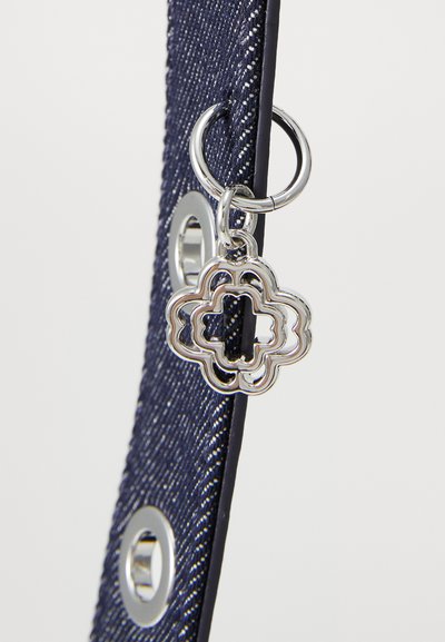 Denimrem med en silverdekorerad charm i en intrikat blommig form, fäst vid en cirkulär metallring och ögla.