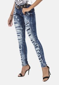 Smalle spijkerbroek in blauwe denim met gescheurde patronen, een vervaagde wassing en subtiele rafels. Gecombineerd met zwarte hoge hakken.