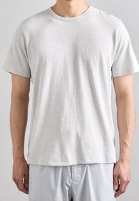 T-shirt grigio chiaro a maniche corte con scollatura a girocollo e spacchi laterali, realizzato in tessuto morbido con una sottile trama.