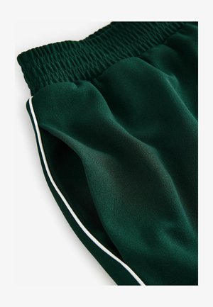 Grüne Sportshorts mit einem gerafften Bund, glatter Textur und weißen Seitenelementen. Nahaufnahme des Stofffalls.