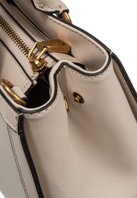 Sac à main en cuir beige avec fermeture éclair dorée, fermoir et boutons-pression, mettant en valeur des coutures détaillées et un bord noir.