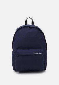 Námořnický modrý batoh Carhartt s přední kapsou na zip a černým úchopem nahoře, vystavený na bílém pozadí.