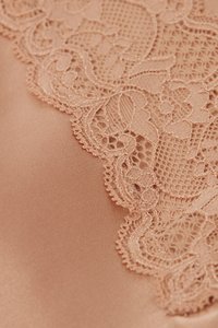 Tela de encaje beige delicada con patrones florales y geométricos sobre un fondo textil liso a juego.