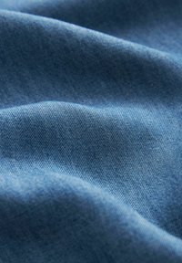 Denim-kangas keskipunaisessa sävyssä, jossa on pehmeä, teksturoitu pinta, jossa on hillittyjä vinonauhakuvioita ja lempeitä taitoksia.
