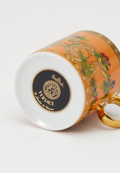 Η κούπα Versace διαθέτει πορσελάνινο σώμα σε πορτοκαλί χρώμα διακοσμημένο με λουλουδένια σχέδια, λευκή βάση και χρυσή λαβή. Στο κάτω μέρος εμφανίζεται το λο�γότυπο και ο σειριακός αριθμός.