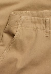 Beige cotton fabric with a smooth texture; features stitched seams and a visible pocket opening; uniform color with minimal design elements.