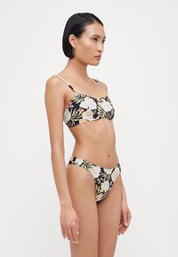 Blomstrete bikini-sett med svart bakgrunn, lyseblå og kremfargede blomster, justerbare stropper og lavt liv med sidedelinger.