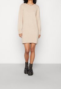 Vestido de suéter de punto beige con mangas largas, puños acanalados y un corte relajado, combinado con botas negras gruesas con cordones.