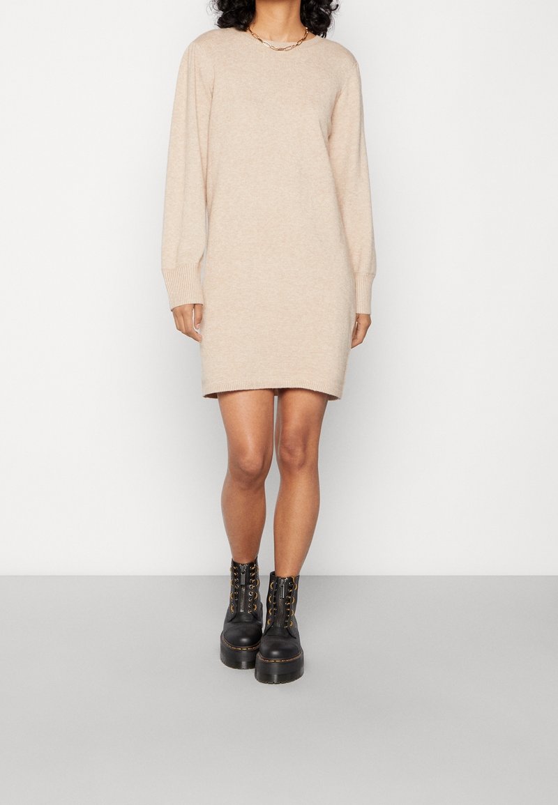 Vestido de suéter de punto beige con mangas largas, puños acanalados y un corte relajado, combinado con botas negras gruesas con cordones.