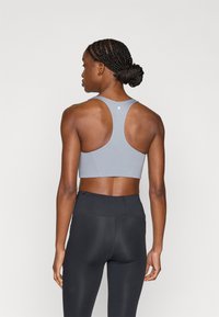 Γκρι αθλητικό σουτιέν με σχέδιο racerback, με λεία υφή και μικρό λογότυπο στην πλάτη. Συνδυάζεται με μαύρο κολάν υψηλής μέσης.