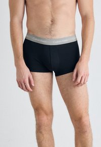 Črne bokserice z sivo elastično pasom, na katerem je napis "Calvin Klein". Narejene iz mehkega, raztegljivega materiala za udobje.