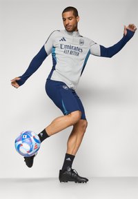 Grey and navy athletic attire with long sleeves and shorts, featuring an Adidas logo and "Emirates Fly Better" text, paired with a multicolored soccer ball.