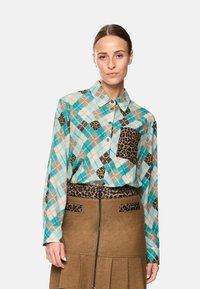Button-up shirt featuring a blue and tan plaid pattern with a leopard-print pocket; paired with a brown skirt having a zipper and pleated detail.