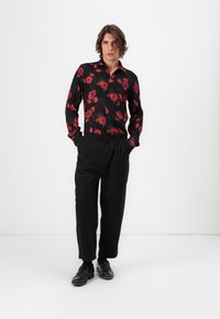 Sort skjorte med rødt blomsterprint, knap-op design, lange ærmer. Sammen med sorte bukser og loafers. Enkel, struktureret stil.
