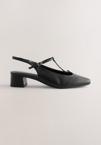 Chaussure slingback noire à petit talon, bout carré, bride en T et boucle latérale réglable sur fond neutre.