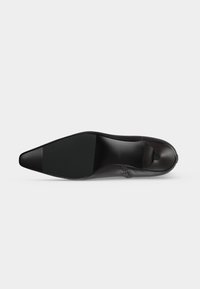 Chaussure formelle en cuir noir vue de la semelle, montrant un bout pointu lisse et brillant ainsi qu’un talon bas.