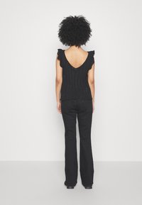 Svart stickad topp med volangärmar, V-skärning bak och vertikalt randmönster, ihopparad med svarta utsvängda byxor och stövlar.