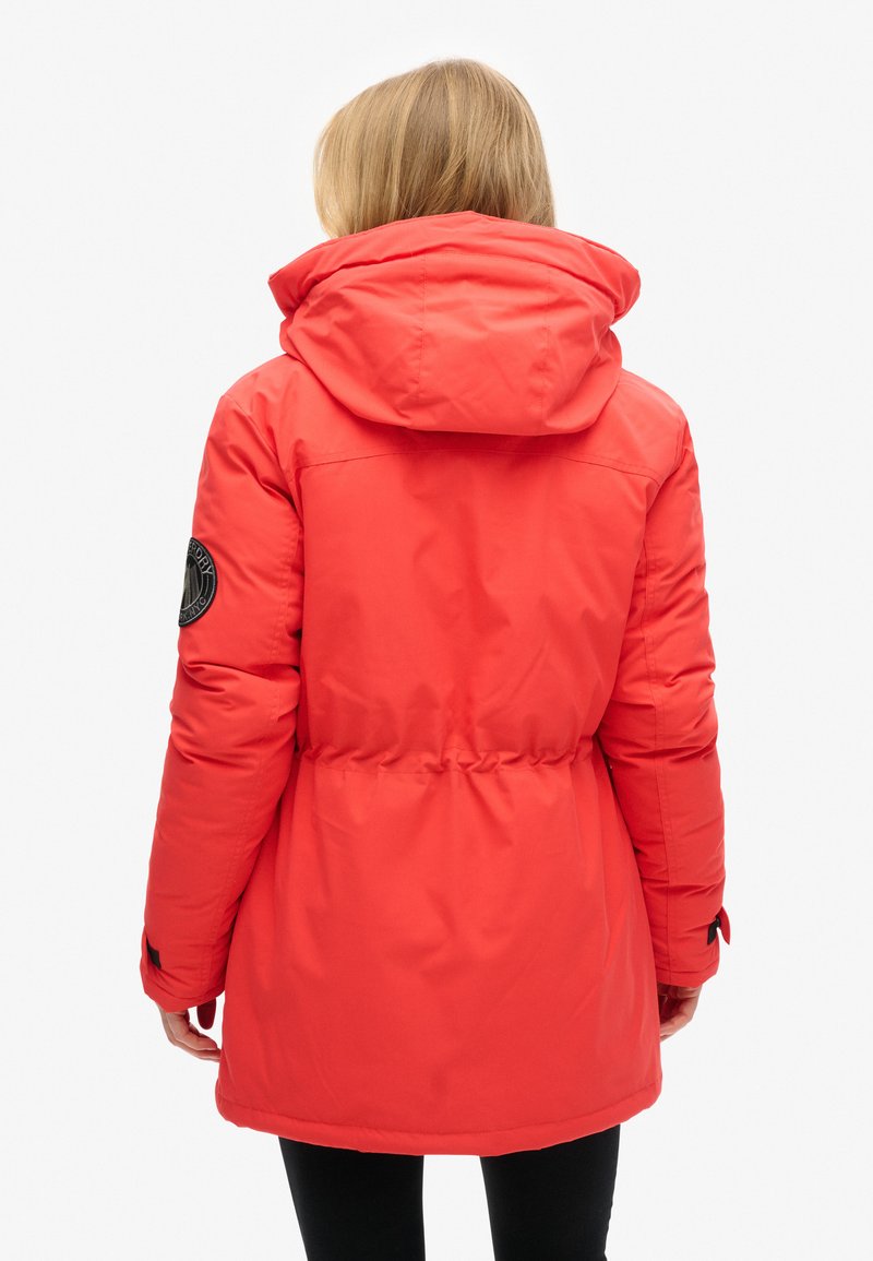 Rote gepolsterte Parka-Jacke mit Kapuze, tailliertem Bund und schwarzem Logopatch am Ärmel. Glattes Material mit weicher Textur.