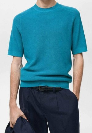 Pull en maille bleu sarcelle à manches courtes, col rond, avec une texture côtelée, associé à un pantalon bleu marine et une ceinture noire.