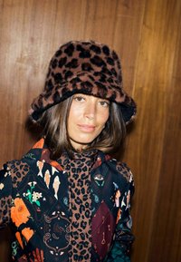 Pălărie tip găleată cu imprimeu leopard, realizată din blană moale, cu bor larg. Modelul poartă o jachetă colorată cu modele florale și geometrice.