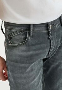 Jeans in denim grigio con una vestibilità dritta, dotati di chiusura a bottone, cinque tasche e lievi sbiadimenti. Il tessuto ha una finitura leggermente testurizzata.
