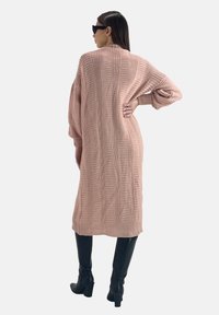 Strickkleid in sanftem Pink mit vertikaler Rippstruktur, langen Ärmeln und knielanger Länge, kombiniert mit schwarzen Kniestrümpfen.