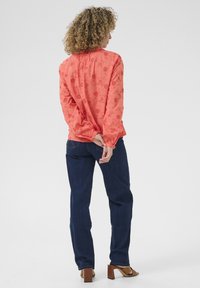 Blusa corallo con ricami floreali, maniche arricciate, abbinata a jeans blu scuro e sandali con tacco quadro marroni.