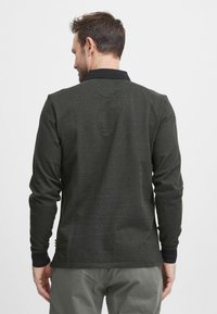 Langermet polo skjorte i mørkegrønn med svart krage. Har et teksturert stoff og ribbede mansjetter. Enkel og funksjonell design.
