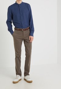 Blå linneskjorta med knappar och ståkrage, kompletterad med bruna chinos och vita sneakers med gumsole.