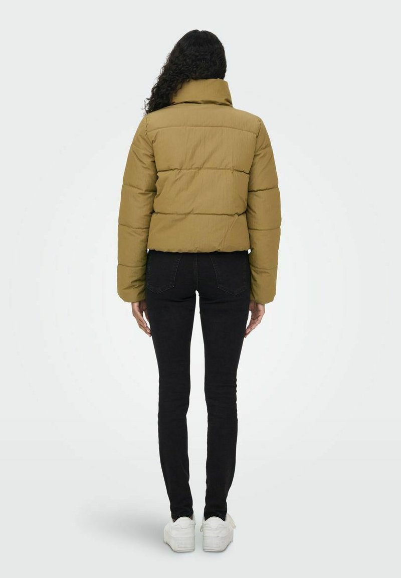 Chaqueta acolchada verde oliva con un cuello alto, secciones cosidas y un diseño corto, combinada con jeans ajustados negros y zapatillas blancas.