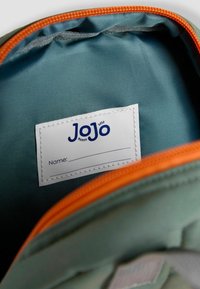 Țesătură interioară verde cu o textură netedă, având un fermoar portocaliu. Include o etichetă albă cu numele "JoJo" pentru personalizare.