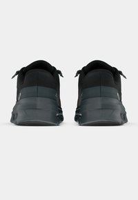 Scarpe sportive nere con una texture liscia, forma arrotondata, suole imbottite e design minimalista con accenti grigi e doppie linguette per il tiraggio.