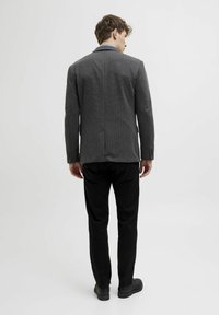 Grau kariertes Sakko mit einem Schlitz, zwei Gesäßtaschen und langen Ärmeln; kombiniert mit schwarzen Hose und dunklen Schuhen.