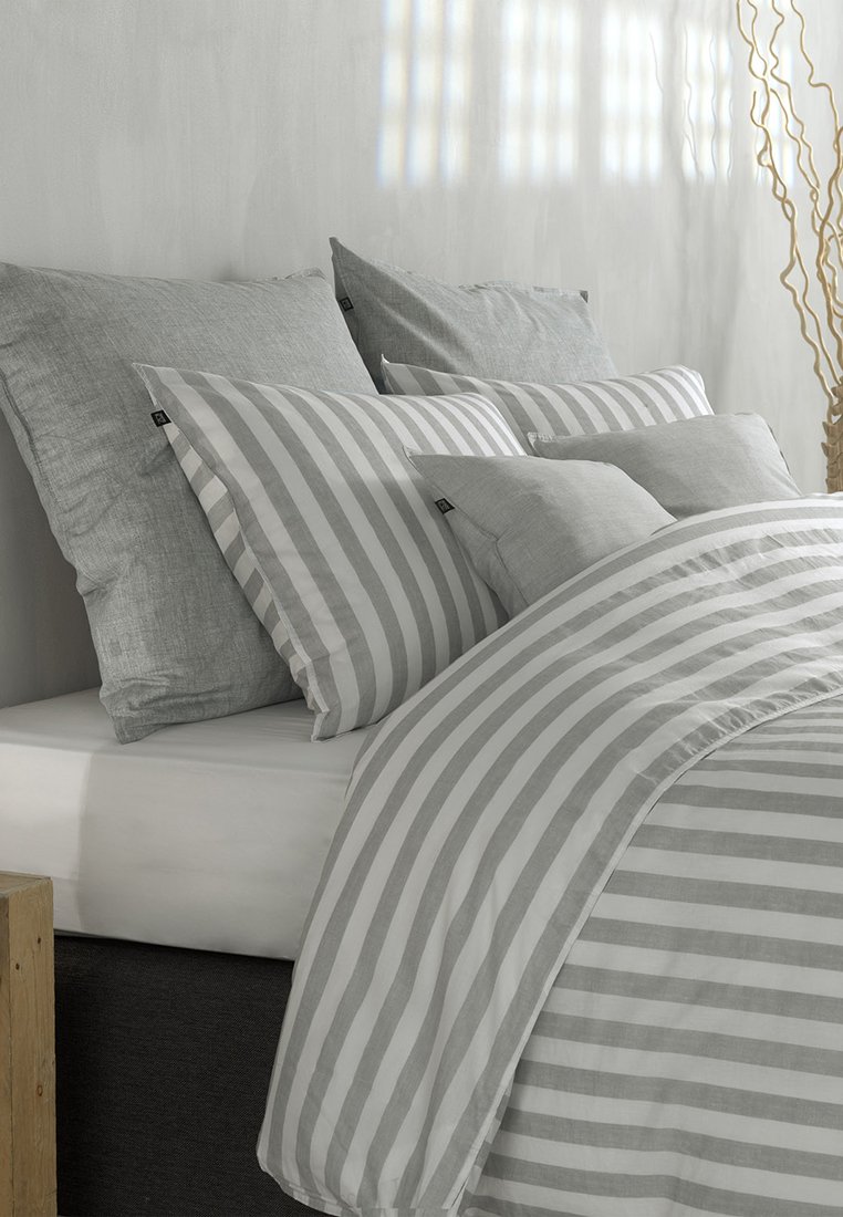 Set di biancheria da letto a strisce grigie con un piumone testurizzato, vari cuscini di dimensioni diverse e un design minimalista su una struttura del letto di colore chiaro.