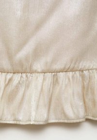 Glittrande beige tyg med en vågig fåll. Slät textur med en subtil glans, med samlad sömnad längs kanten.