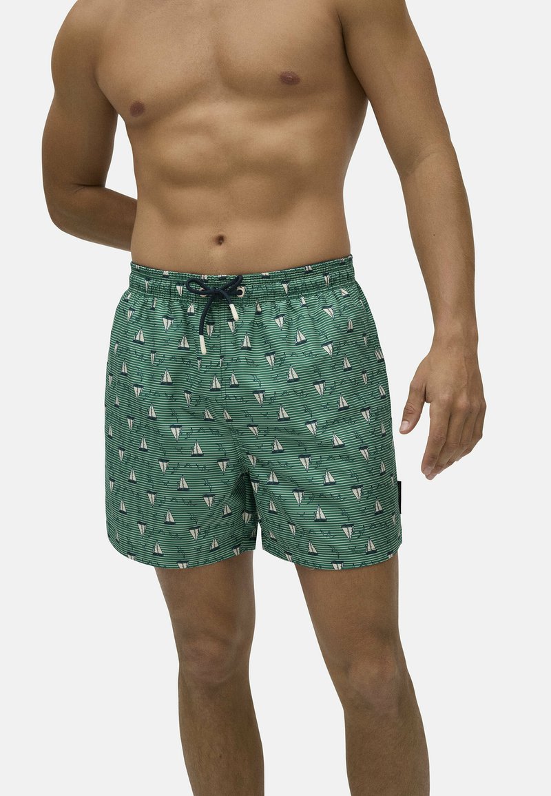 Bañador verde con un patrón de veleros, cinturilla elástica y cordón. El material parece ligero y suave, con un ajuste relajado.