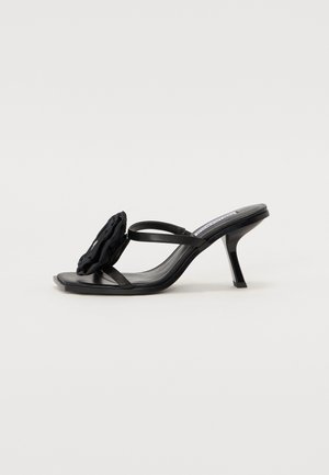 Sandales à talons noirs avec une finition lisse et brillante, dotées d'un accent floral froncé sur l'orteil et de fines brides pour un design minimaliste.