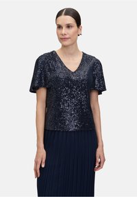 Niebieska top z cekinami, z dekoltem w serek i krótkimi rękawami, z teksturowanym wzorem; w komplecie z plisowaną niebieską spódnicą.