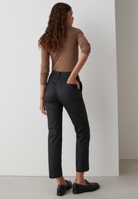 Black denim pants with a straight fit, featuring back pockets and a high waist. Paired with a fitted brown top and black loafers.