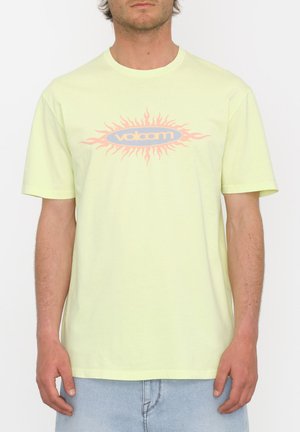 Camiseta de algodón amarilla clara con mangas cortas, que presenta un gráfico central de un patrón radial de sol y el texto "volcom" en azul y rosa.