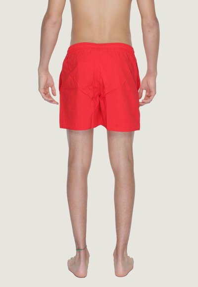 Costumi da bagno rossi con vita elastica, lunghezza fino alla coscia e una texture liscia. Mostrati da dietro su uno sfondo semplice.