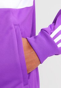 Lila långärmad sweatshirt med ett vitt horisontellt rand, texturerad tyg och en känguruficka med ribbade muddar.