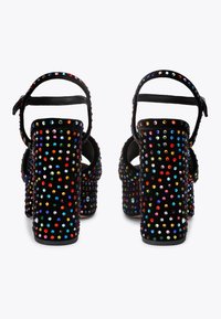 Czarne sandały na wysokim obcasie pokryte wielokolorowymi kryształkami, z paskiem na kostkę i zamszową fakturą oraz masywnym obcasem.