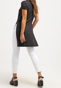 Tunic nera a maniche corte con un orlo posteriore leggermente più lungo, abbinata a jeans skinny bianchi e sandali con tacco spesso neri.