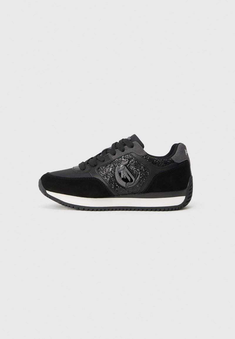 Adidași negri cu sireturi negre, panou din suede și sclipici, talpă intermediară albă și talpă exterioară texturați negri, vedere laterală pe un fundal deschis.