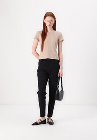 Beige stripete topp med korte ermer, svarte skreddersydde bukser, svarte leiligheter med detaljer, og en liten svart håndveske med nagler. Enkel, tettsittende design.