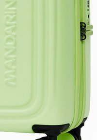Valise rigide verte à surface rainurée, fermeture éclair et roues noires. Nom de la marque "Mandarina" embossé sur la surface.